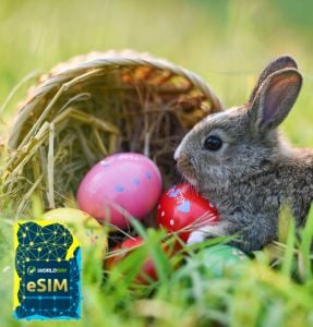 A rabbit sits beside a basket of colorful Easter eggs in a grassy field, with the WorldSIM logo and an image of a WorldSIM eSIM card prominently displayed