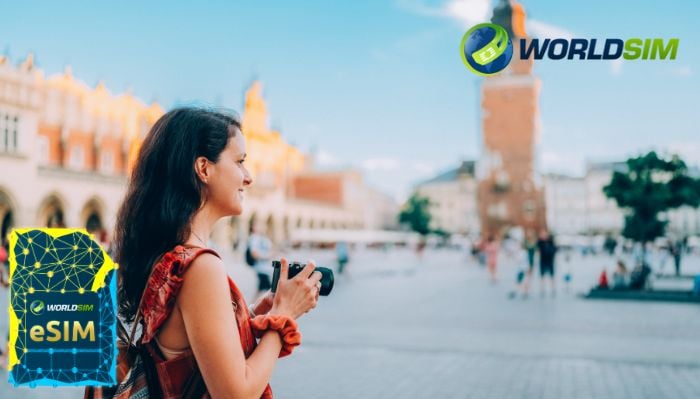 A woman with long dark hair, wearing a red dress and holding a camera, stands in a European city square with historic buildings in the background. The image also features the WorldSIM logo and an eSIM card graphic