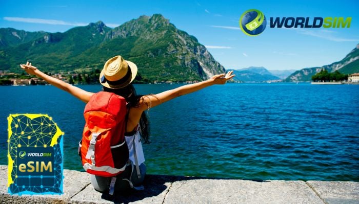 Prepaid eSIM Plans: The Future of Flexible and Affordable Travel Connectivity A traveler with a backpack enjoys a scenic view of a lake and mountains, with arms outstretched, featuring the WorldSIM logo and an image of a WorldSIM eSIM card