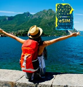 A traveler with a backpack enjoys a scenic view of a lake and mountains, with arms outstretched, featuring the WorldSIM logo and an image of a WorldSIM eSIM card