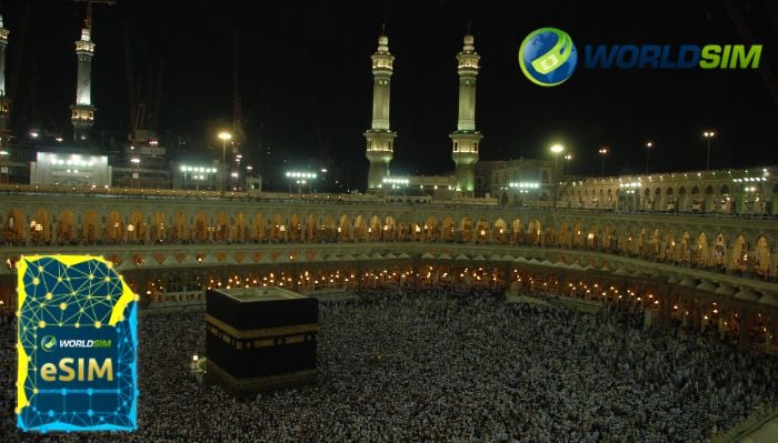  The Grand Mosque in Mecca filled with pilgrims performing Hajj, highlighted by the WorldSIM logo and an image of a WorldSIM eSIM card